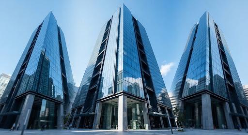 A modern glass-and-steel skyscraper reflecting a clear blue sky, representing the corporate financial services sector.